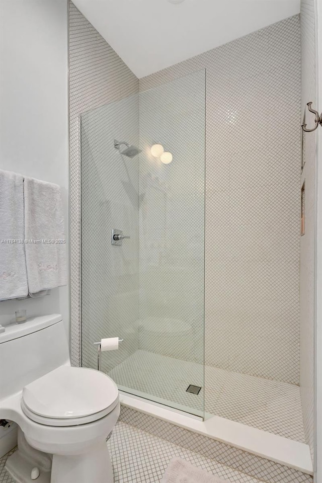 bathroom featuring toilet, tile patterned flooring, and a tile shower