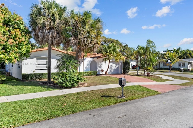 view of front facade with a front yard, a tiled roof, a garage, and stucco siding