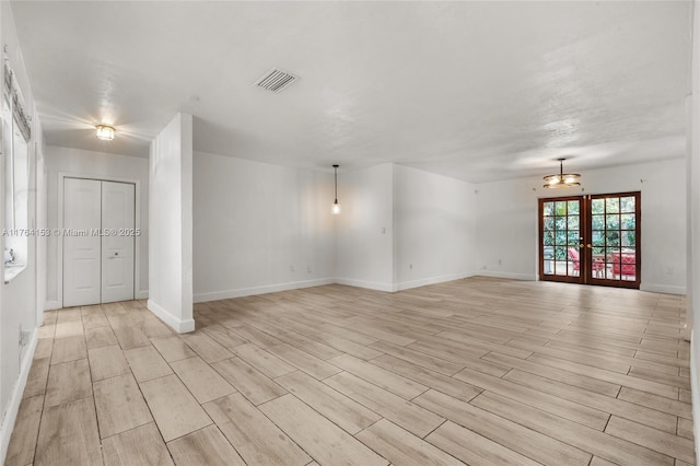 empty room with light wood-style floors, visible vents, french doors, and baseboards