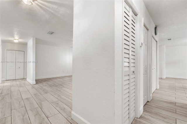 hallway with light wood-style flooring, visible vents, and baseboards