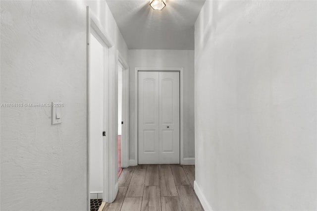 corridor featuring light wood finished floors and baseboards