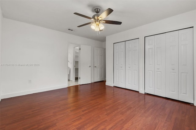 unfurnished bedroom featuring visible vents, two closets, a ceiling fan, wood finished floors, and baseboards