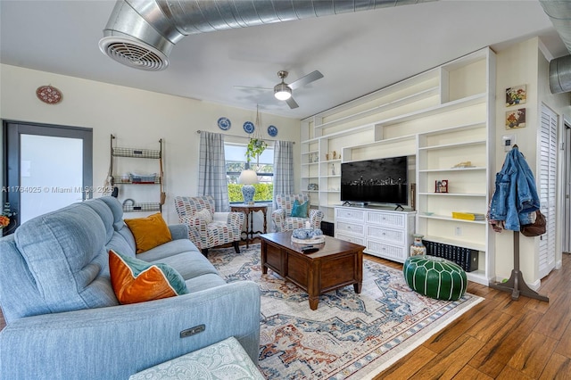 living area featuring built in features, wood finished floors, visible vents, and ceiling fan