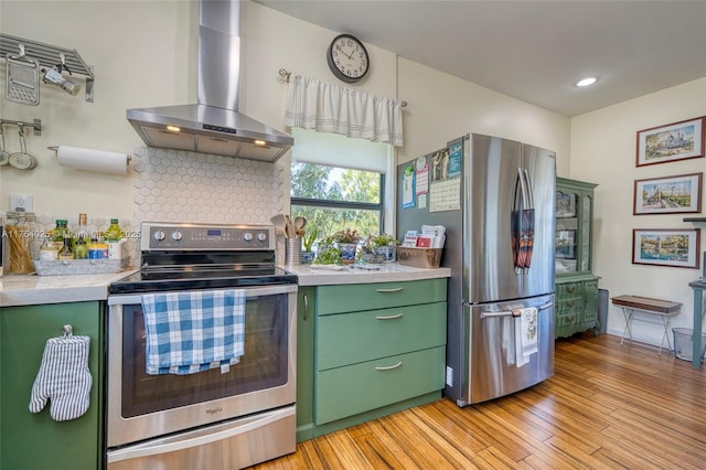 kitchen with ventilation hood, light countertops, light wood-style flooring, appliances with stainless steel finishes, and green cabinetry