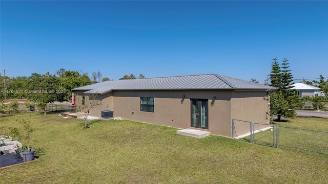 rear view of house featuring central air condition unit, stucco siding, a yard, and a gate