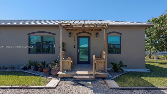 property entrance featuring fence, stucco siding, metal roof, a yard, and a standing seam roof