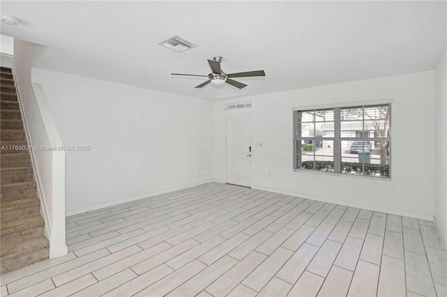 empty room featuring visible vents, stairway, ceiling fan, and wood finished floors