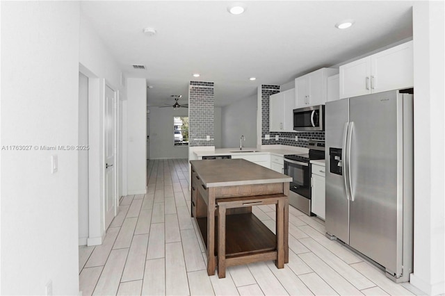 kitchen featuring decorative backsplash, a peninsula, stainless steel appliances, a ceiling fan, and a sink