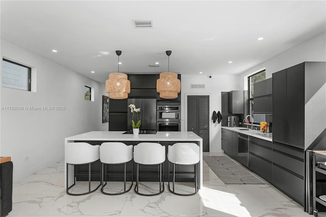 kitchen with multiple ovens, visible vents, modern cabinets, a sink, and a kitchen breakfast bar