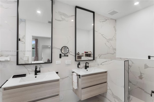 full bathroom with visible vents, two vanities, marble finish floor, tile walls, and a sink