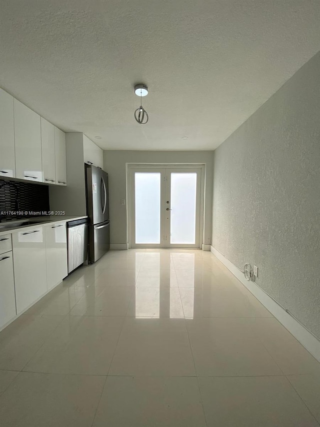 kitchen featuring appliances with stainless steel finishes, french doors, a textured wall, a textured ceiling, and white cabinetry