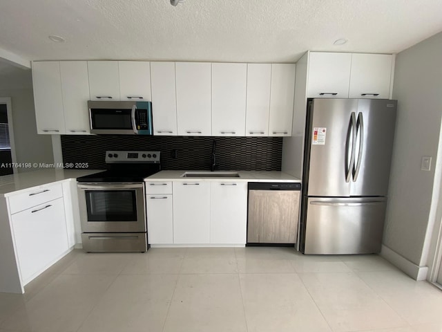 kitchen with backsplash, light countertops, stainless steel appliances, white cabinetry, and a sink