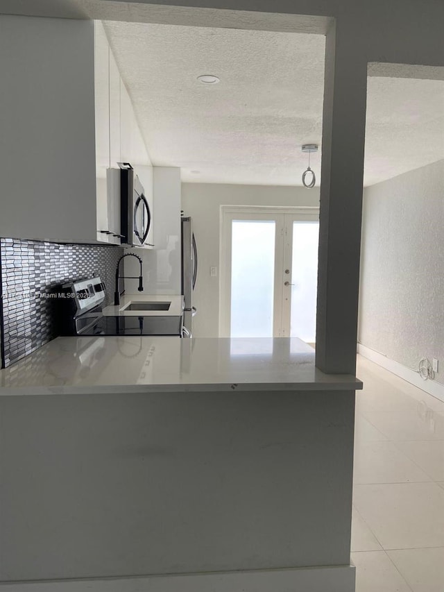 kitchen with light tile patterned floors, decorative backsplash, a peninsula, a textured ceiling, and stainless steel appliances