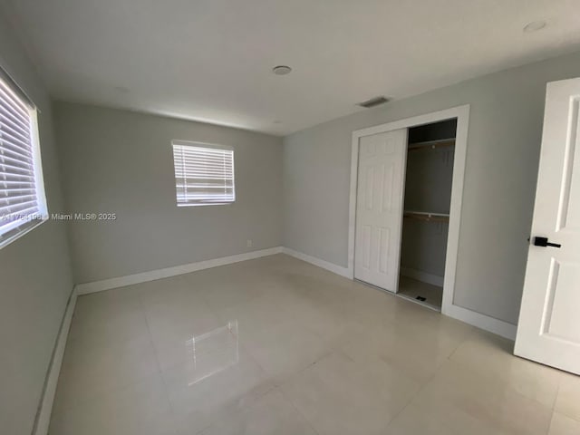 unfurnished bedroom with multiple windows, baseboards, visible vents, and a closet