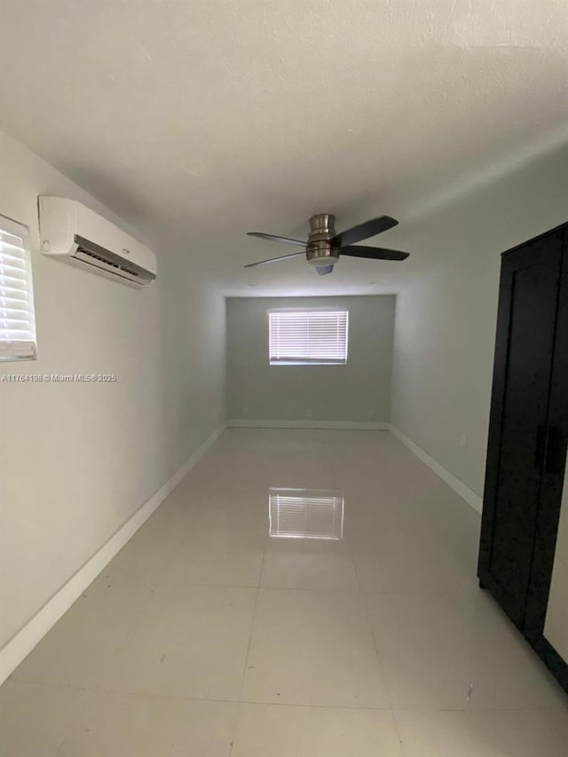 unfurnished room featuring light tile patterned floors, ceiling fan, baseboards, and a wall unit AC