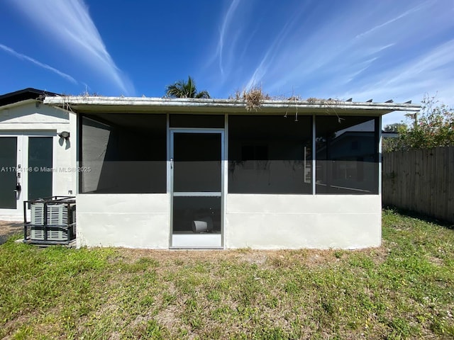 rear view of house featuring stucco siding, fence, a yard, and a sunroom