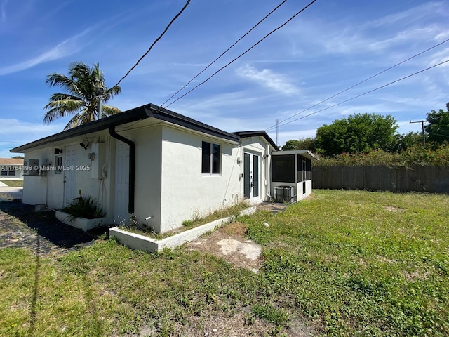 view of home's exterior with fence, a yard, a sunroom, stucco siding, and central air condition unit