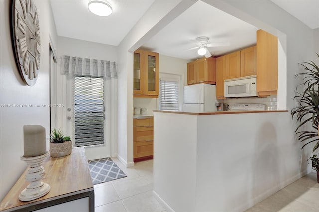 kitchen featuring white appliances, light tile patterned floors, a ceiling fan, a peninsula, and glass insert cabinets