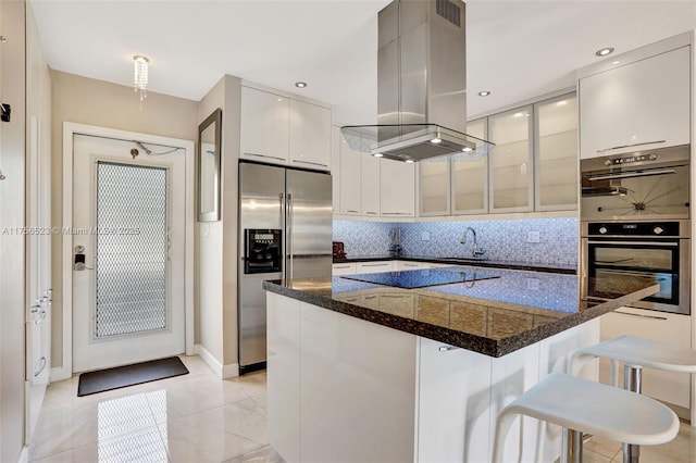 kitchen featuring a breakfast bar, decorative backsplash, island exhaust hood, stainless steel appliances, and white cabinetry