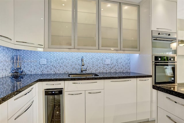 kitchen with dark stone countertops, beverage cooler, a sink, decorative backsplash, and white cabinets