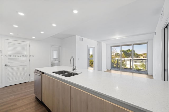 kitchen with a sink, light stone counters, stainless steel dishwasher, wood finished floors, and recessed lighting