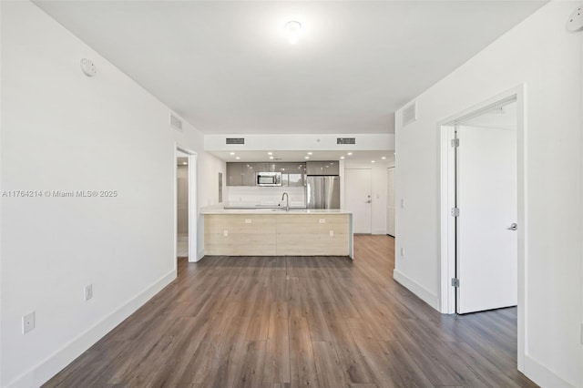 unfurnished living room with a sink, visible vents, and dark wood-style floors