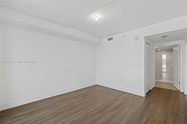 empty room with dark wood-style floors, visible vents, and baseboards