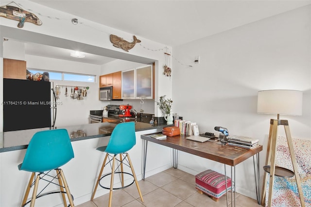 kitchen with a kitchen breakfast bar, dark countertops, appliances with stainless steel finishes, a peninsula, and light tile patterned floors