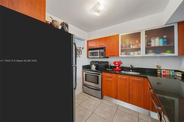 kitchen with brown cabinets, a sink, stainless steel appliances, light tile patterned floors, and glass insert cabinets