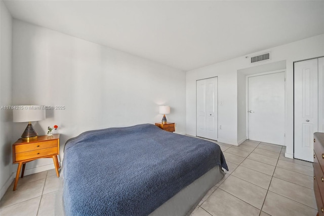 bedroom with visible vents, multiple closets, baseboards, and light tile patterned flooring