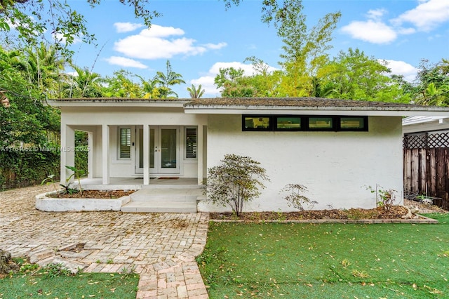 view of front facade featuring french doors, stucco siding, fence, and a front lawn