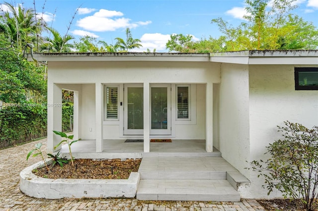 view of exterior entry with stucco siding and covered porch