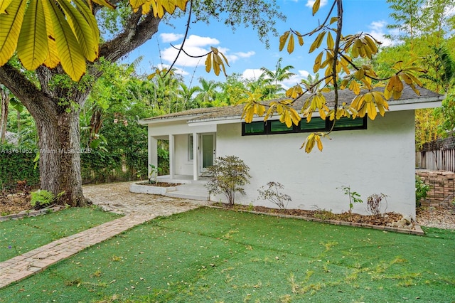 exterior space featuring stucco siding, fence, and a front lawn