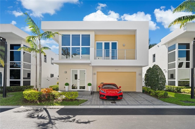 contemporary house featuring stucco siding, decorative driveway, french doors, an attached garage, and a balcony