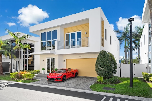 modern home with fence, stucco siding, french doors, a balcony, and a gate