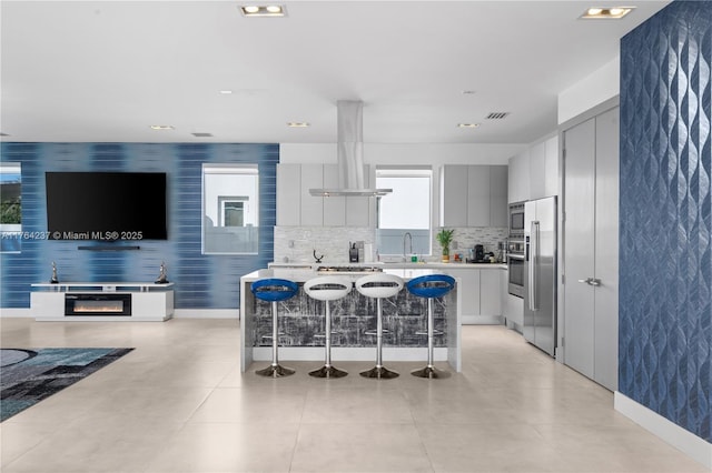 kitchen featuring island exhaust hood, modern cabinets, wallpapered walls, and stainless steel appliances