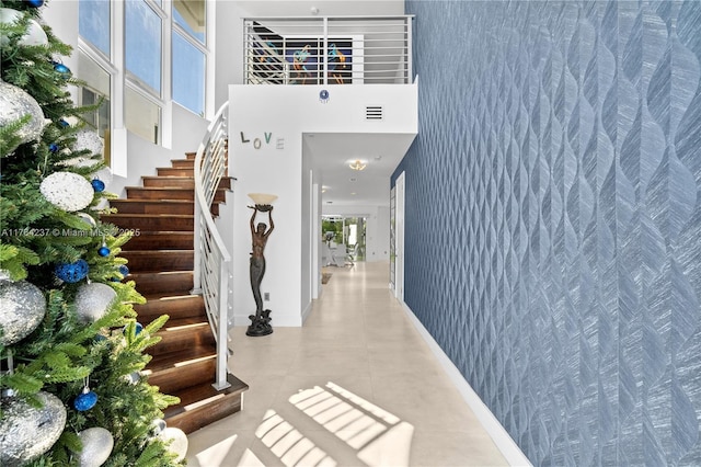 tiled foyer featuring stairway, baseboards, visible vents, and a towering ceiling