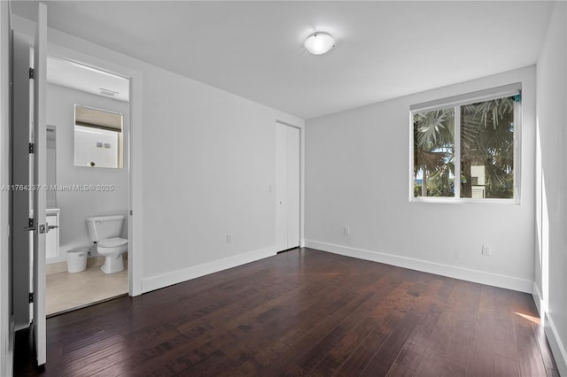 unfurnished bedroom with visible vents, ensuite bathroom, dark wood-type flooring, and baseboards