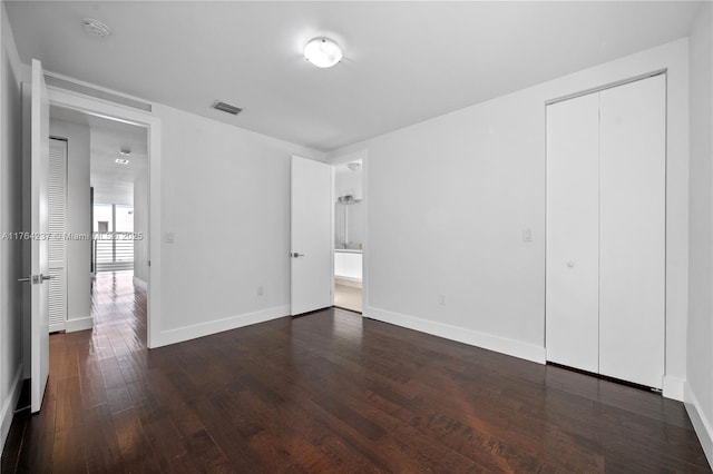 unfurnished bedroom with visible vents, ensuite bath, dark wood-style floors, a closet, and baseboards