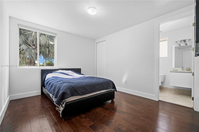 bedroom featuring a closet, ensuite bathroom, baseboards, and hardwood / wood-style floors