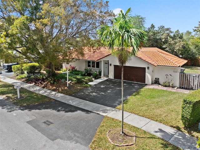 view of front facade featuring fence, a tile roof, stucco siding, driveway, and an attached garage