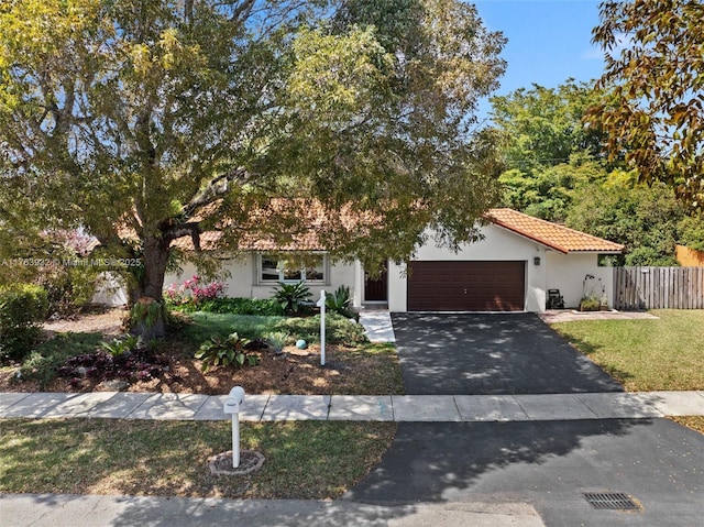 view of front of house featuring fence, a tiled roof, stucco siding, a garage, and driveway