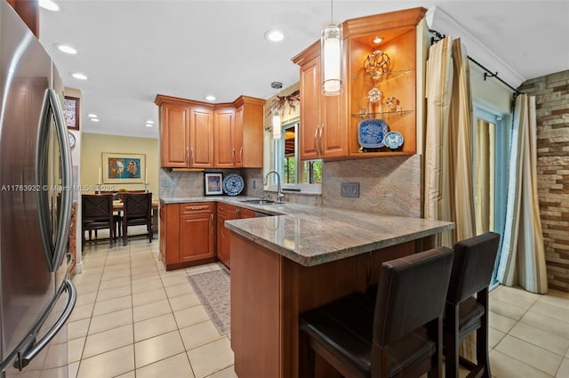 kitchen featuring a sink, a kitchen breakfast bar, freestanding refrigerator, a peninsula, and crown molding