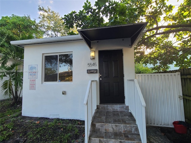 doorway to property featuring stucco siding and fence