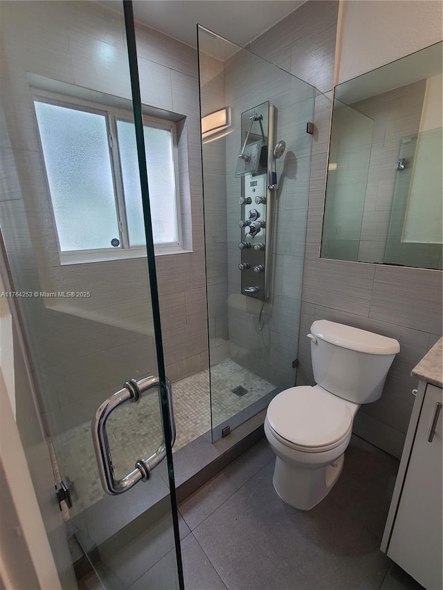 bathroom with tile patterned floors, toilet, tile walls, tiled shower, and vanity