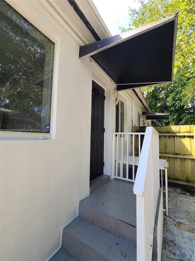 view of exterior entry with fence and stucco siding