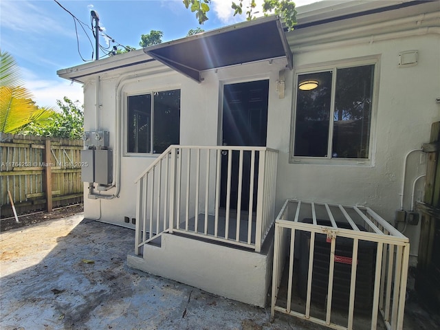 doorway to property featuring stucco siding and fence