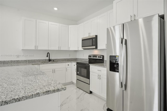 kitchen with light stone counters, a sink, appliances with stainless steel finishes, white cabinetry, and marble finish floor