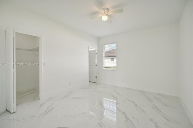 unfurnished bedroom with baseboards, a ceiling fan, marble finish floor, and a spacious closet