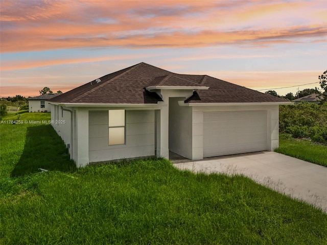 ranch-style home featuring stucco siding, a lawn, roof with shingles, and an attached garage